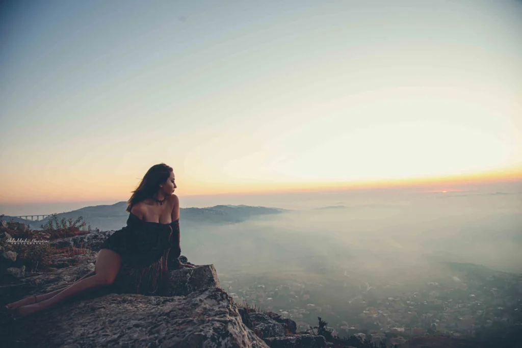 Woman sitting on a rocky cliff during sunset with misty horizon