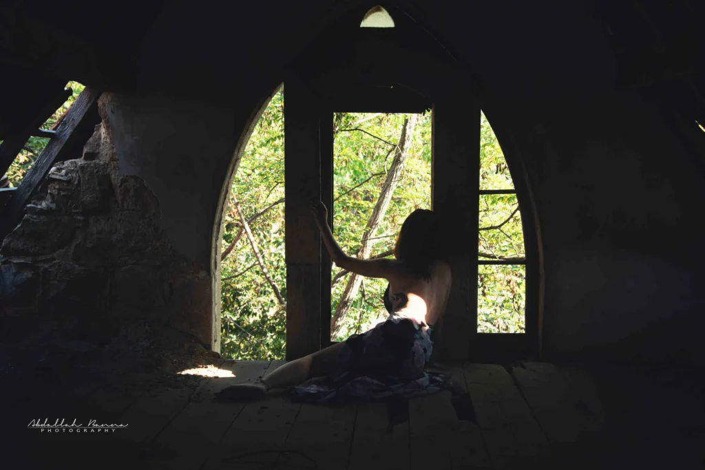 Woman sitting on rocky terrain with head resting on knees against hazy background.