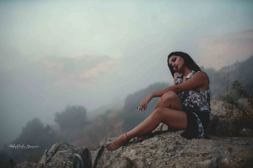 Woman sitting on rocks with eyes closed in misty early dawn light.