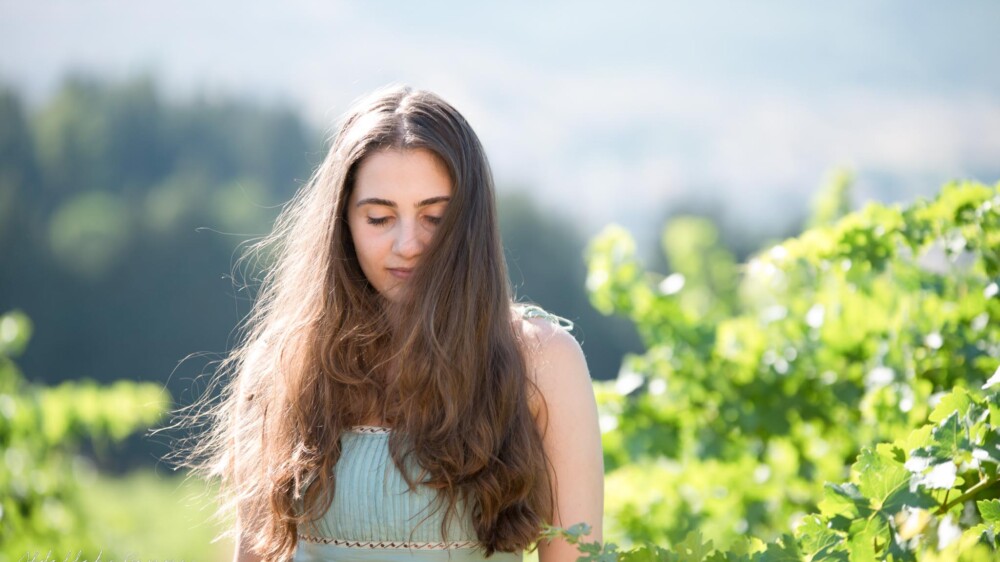 Woman with long hair walking through a vineyard.