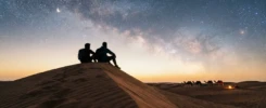 لقطة سينمائية لصديقين يجلسان فوق كثبان رملية تحت سماء مرصعة بالنجوم تعبيراً عن رفيق الدرب